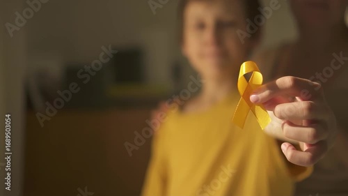 Close-up of yellow satin cancer awareness ribbon held by teenage boy, showing support for pediatric cancer patients and research.