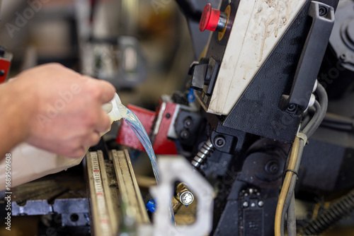 Adding coolant to a large hacksaw for metal and wood. Industrial machine maintenance