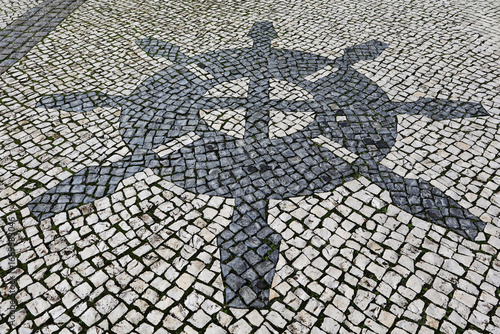 Traditional pattern cobblestone pavement (calçada portuguesa) with steering wheel of the ship in Faro, Algarve, Portugal