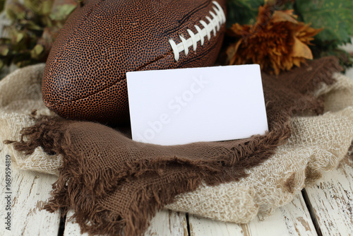 Blank white horizontal card mockup on fabric backing with rugby ball and dried maple leaves, soft natural light.