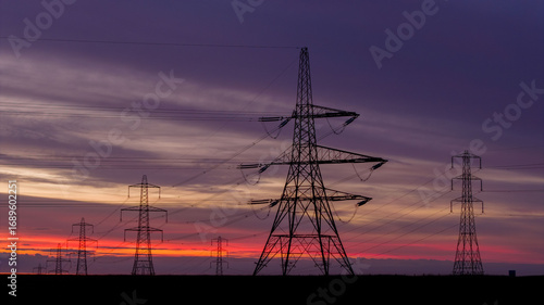 Electricity Pylons at Sunrise with Vibrant Sky in Rural Landscape