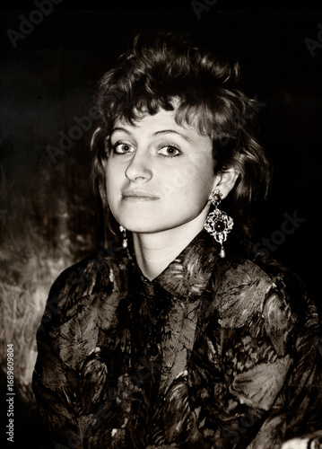 Vintage half-turned portrait of an extravagant beautiful young girl, dressed in the fashion of the 80s. Retro photo from 1987.