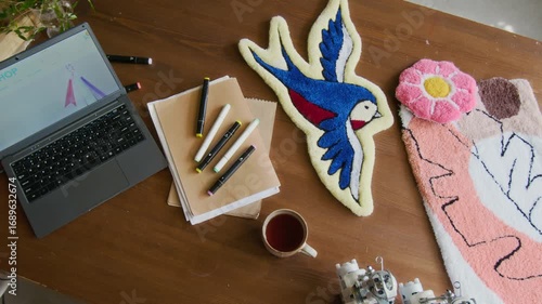 Top view shot of laptop and colorful handmade rugs on wooden table in rug tufting workshop, small business concept, copy space