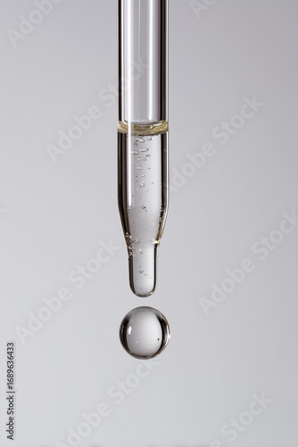 Close-up of a glass pipette releasing transparent liquid, for skincare or pharmaceutical use.