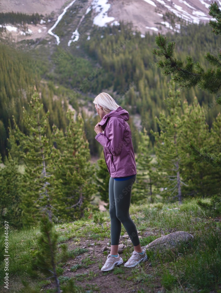 Naklejka premium Blonde Athletic Woman Admiring Mountain Views on Autumn Evening Hike in Forest Path
