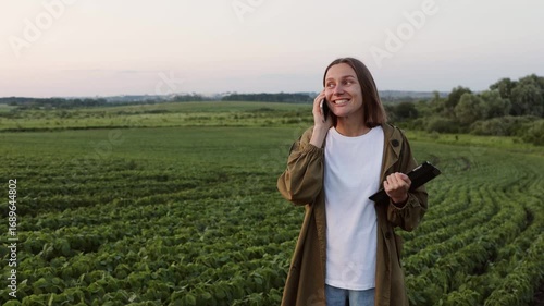 Modern agribusiness. Happy female farmer with digital tablet, talks on smartphone after examine and check in soybeans plants at field. Agronomist controls growth of harvest. Smart farming technology.