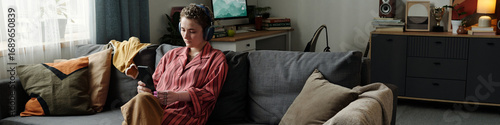 Fotografie Caucasian young adult woman sitting on sofa using smartphone with headphones, ap