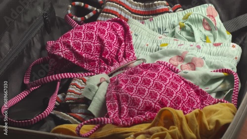 Close-up of woman placing a swimsuit into a suitcase and preparing for vacation at home, recorded with ambient sound.