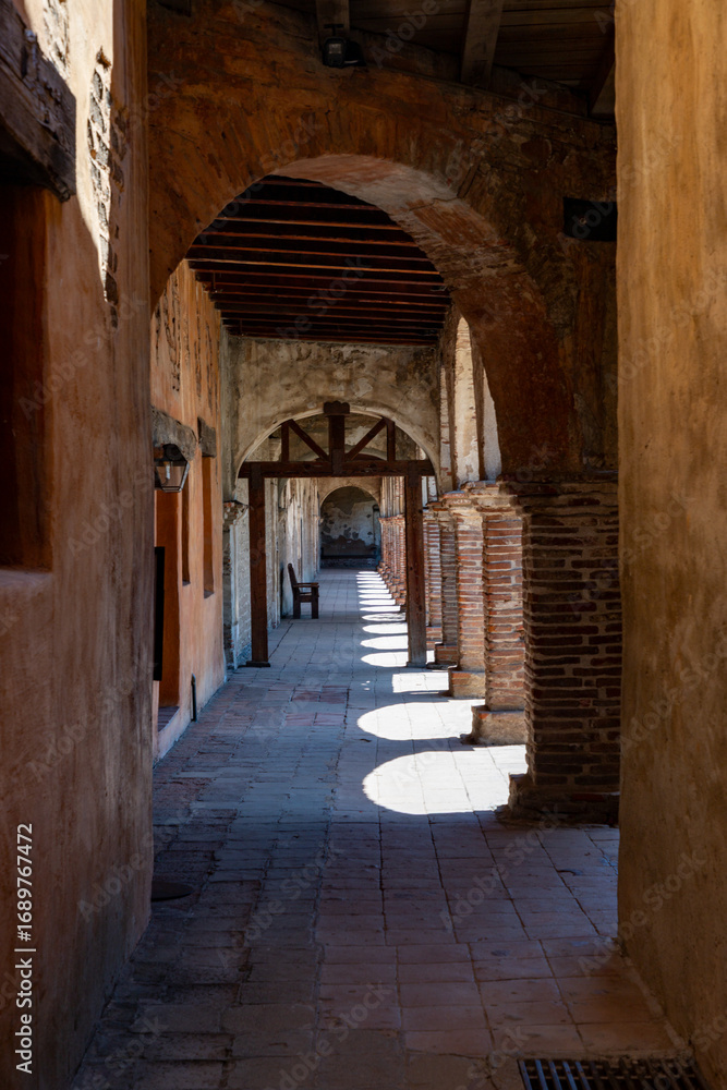 Obraz premium Sunlit Colonial Corridor with Arches and Wooden Chair