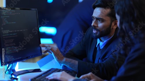 A male and female programmer collaborate on a software project in their tech office. They are working together as a team to write and review code after hours to meet a deadline.