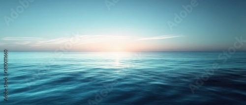 Serene calm ocean waves under soft pastel sunrise with clear blue sky and gentle light reflecting on water surface