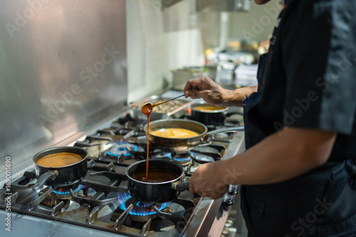 Canvastavla The image shows a chef working in a professional kitchen, meticulously stirring a sauce in a pot on a gas stove