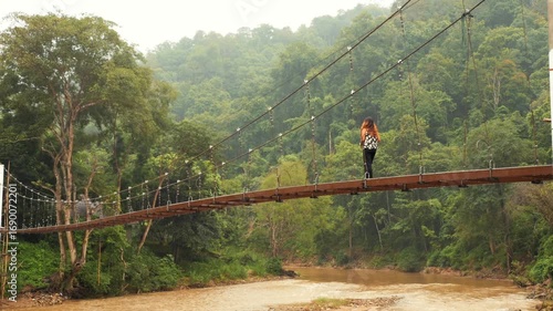 Young Woman Walking on Suspension Bridge Over River in Tropical Jungle of Thailand