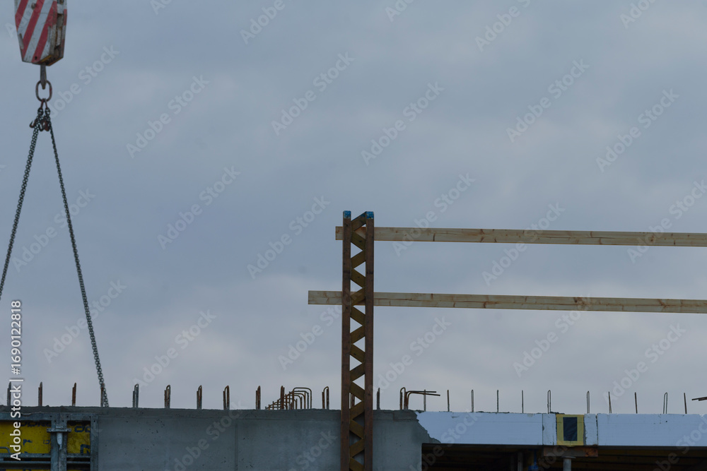 Obraz premium A construction site showcasing a crane lifting wooden beams against a cloudy sky.