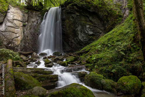 long exposure of a scenic waterfall in a mossy green valley in Switzerland