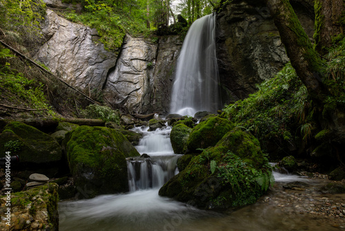 long exposure of a scenic waterfall in a mossy green valley in Switzerland