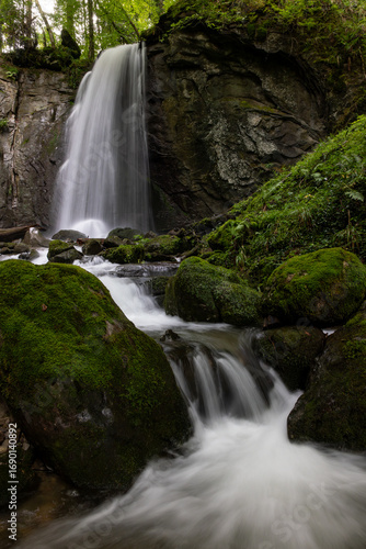long exposure of a scenic waterfall in a mossy green valley in Switzerland
