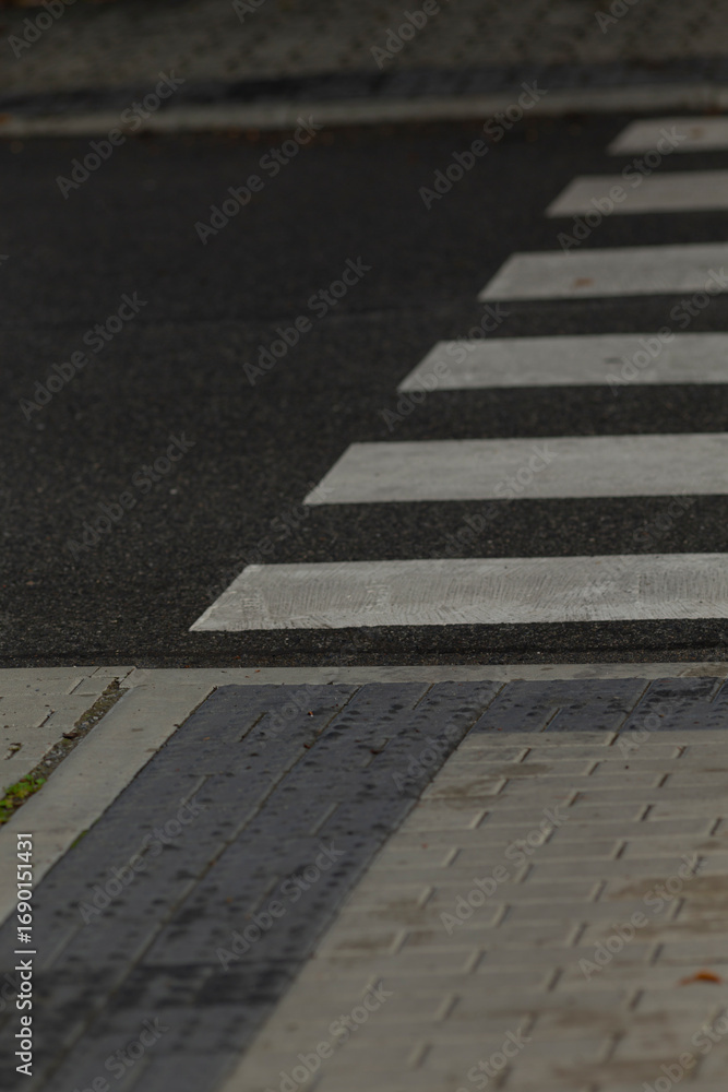 Obraz premium A close-up view of a pedestrian crosswalk featuring white stripes against dark pavement and textured tiles, highlighting urban infrastructure.