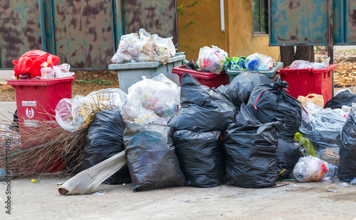 Garbage bins and containers full, overflowing, with bags falling on ground in residential area of Bordeaux, France, in a green container.