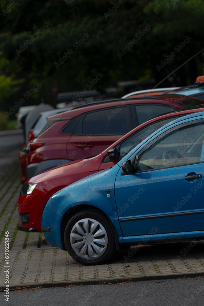 Naklejka premium A vibrant display of parked cars in various colors including blue and red, showcasing modern automotive design in an urban setting.
