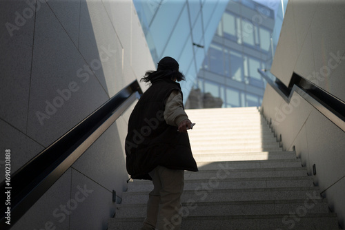 A person is seen walking up a set of stairs while a tall building stands prominent in the background, creating an interesting contrast
