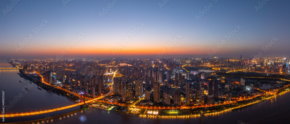 Fototapeta premium Wuhan, China cityscape at twilight with glowing city lights illuminating the urban landscape and a river reflecting the sky's warm hues.