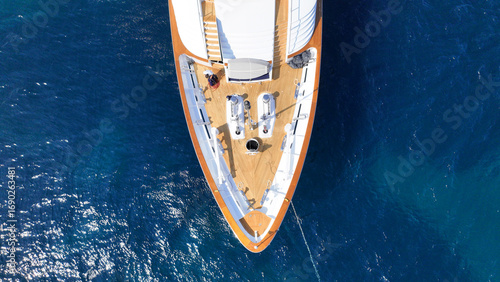 Aerial drone top down photo of luxury yacht with wooden deck anchored in deep blue Aegean sea, Mykonos island, Cyclades, Greece