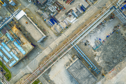 Aerial view of an industrial plant layout showing buildings, pipe racks, and various construction materials on the ground.