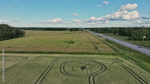 Aerial footage of a rural countryside landscape in Estonia, featuring golden wheat fields, a curving road, Tallinn-Tartu highway and unique crop circles. Agriculture, nature, and travel concept. 
