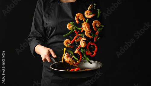 Chef tossing shrimp and vegetables in a frying pan against dark backdrop