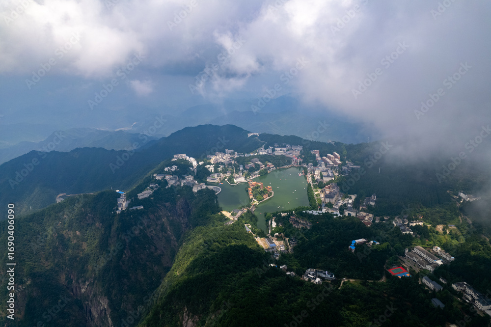 Naklejka premium Jiugong Mountain Xianning China overlooks a serene lake surrounded by lush green mountains and scattered buildings under a partly cloudy sky.