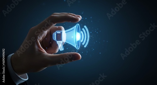 A businessmans hand holding a glowing blue megaphone icon, symbolizing announcement, communication, and marketing strategies in a digital world with a dark blue background