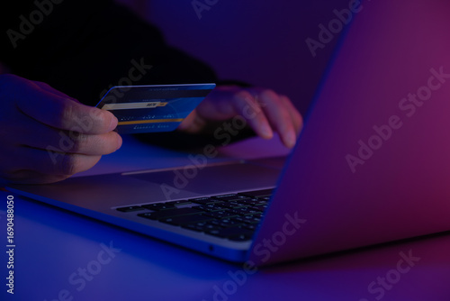 Hacker holding a credit card while accessing a system with a laptop. Concept of cybercrime, online fraud, identity theft, hacking, and digital security risk