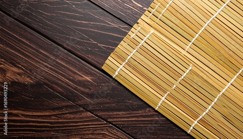 Traditional bamboo sushi mat resting diagonally on a dark, rustic wooden tabletop, creating a textured and serene background for Asian cuisine