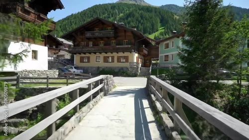 Scenic view of a wooden bridge leading to charming alpine houses surrounded by lush greenery and mountains