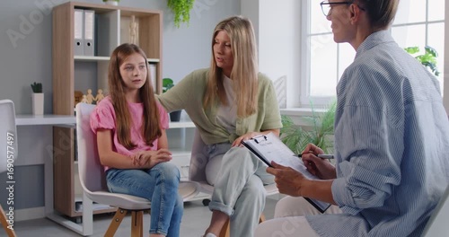 A psychologist leads a therapy counseling session with a child, mother, and daughter, guiding conversation in an office and offering empathy and support. Family meets with the therapist today.