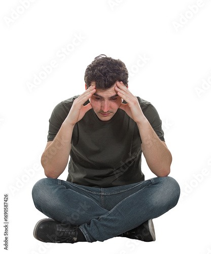 Upset and depressed young man sitting on the floor with hands pointed to forehead looking down thoughtful in sorrow, isolated on transparent background with copy space