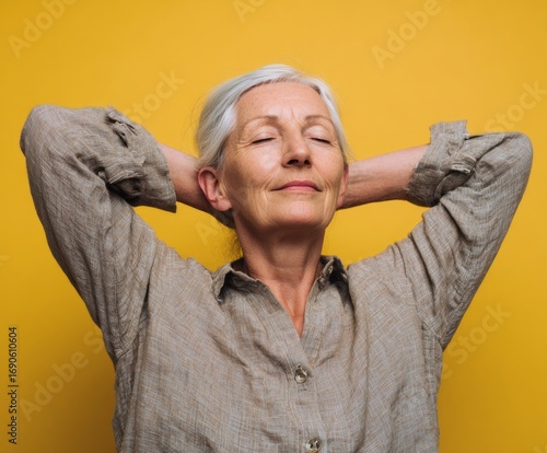 A serene senior woman reclines in a relaxed pose against a vibrant yellow backdrop, showcasing a tranquil mood and effortless style.