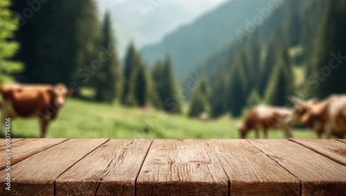 In a serene rural setting with hills and trees, a vacant wooden table sits in front of a soft-focus scene of cows grazing in a green pasture, beneath a clear sunny sky, making it an ideal backdrop