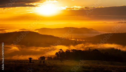 Golden sunrise over mountain landscape, sunlight rays streaming through morning mist, serene valley