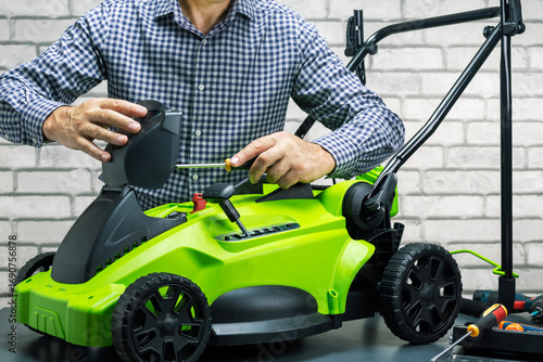 Technician, man in uniform is repairing a electric cordless lawn mower on workbench. Small business.