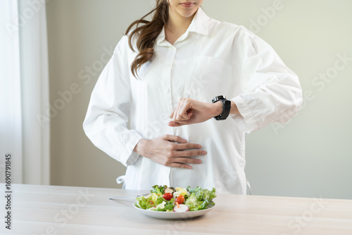 Intermittent fasting, diet healthy asian young woman dietary watching wrist watch, stomach ache, temptation hungry of brunch food in morning, waiting time to eat salad but not yet time first meal.