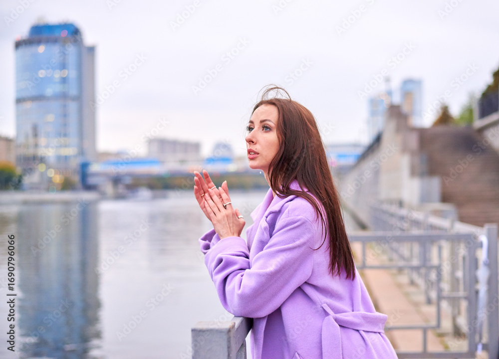 Fototapeta premium There is a woman in a purple coat standing on the pier, with a view of the pond. She has a beautiful and slender figure.