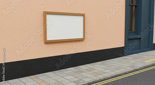 Blank framed sign on a textured wall with a sidewalk view.