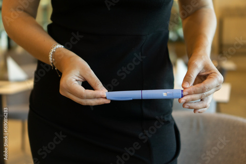 Fotografie A woman in a black dress holding an ozempic pen, concept of medical treatment, modern healthcare, and weight loss solutions