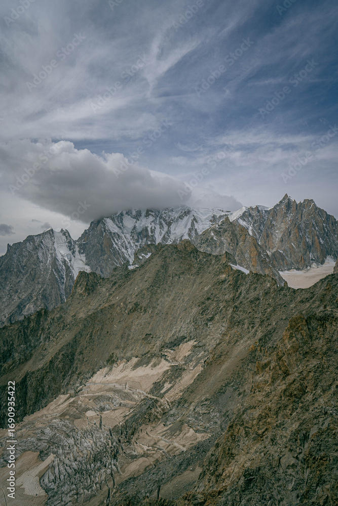 Obraz premium Alps mountain panorama with towering granite spires and snow patches beneath storm clouds creating dramatic high altitude scenery