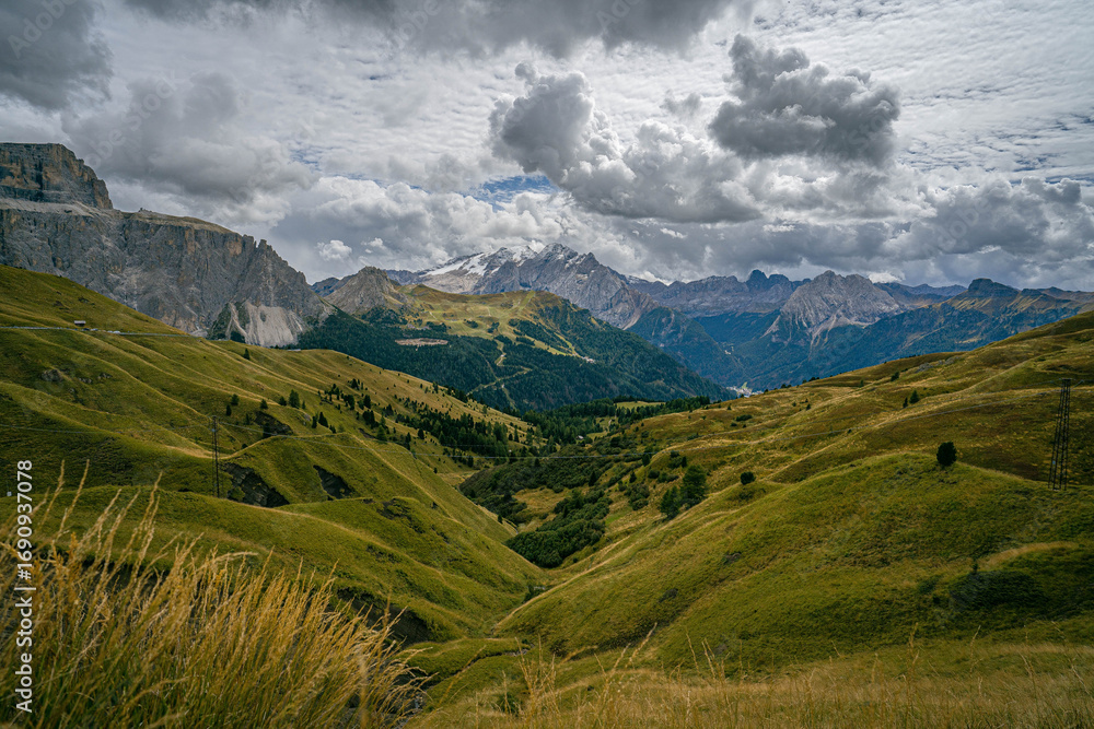 Obraz premium Dolomites alpine valley with grassy slopes, rocky cliffs and high peaks under storm clouds creating dramatic mountain landscape scene