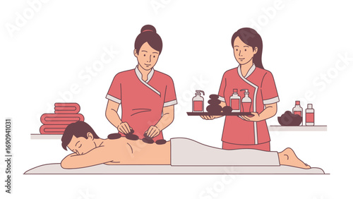 Two female spa therapists performing a hot stone massage on a relaxed client lying on a massage table with towels and oils nearby