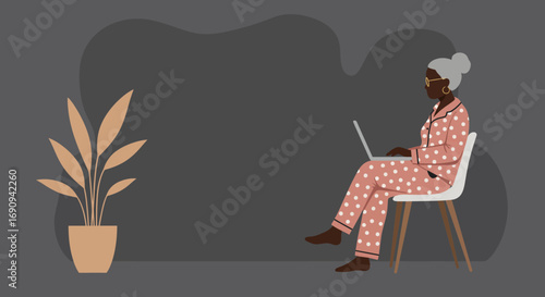 Relaxed senior Black woman in pajamas uses laptop at home, illustrating remote work, digital connection, and comfortable modern living.