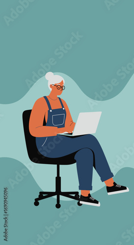 Smiling senior woman in overalls and glasses working on a laptop in a modern setting. Illustrates digital engagement, remote work, and independent learning.